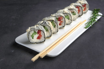 Sushi roll with chopsticks on a white plate close up. Gray background and rosemary