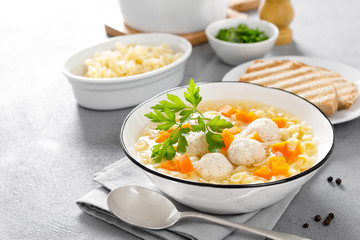 Hot chicken soup, broth with meatballs, carrot, pasta and fresh parsley