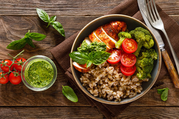 Chicken lunch bowl with broccoli, fresh tomato, pearl barley porridge and basil pesto on wooden rustic background