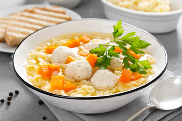 Hot chicken soup, broth with meatballs, carrot, pasta and fresh parsley