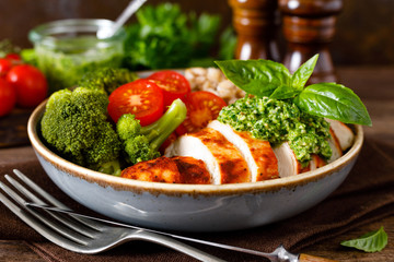 Chicken lunch bowl with broccoli, fresh tomato, pearl barley porridge and basil pesto on wooden...