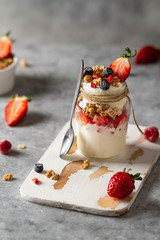 Jars with yogurt, berries and granola with spoon. Healthy breakfast with greek yoghurt.
