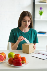 girl with allergy holding napkins while sitting at table with fruits and vegetables