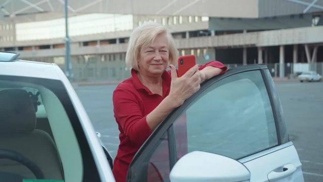 Happy senior woman stand near car use red cell phone smile businesswoman blonde people smartphone cellphone communication internet search lady mobile browse network online slow motion