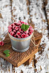 Frozen raspberries in a backet on wooden background.