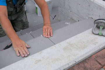 Tiler hands working on a new house entrance, local and professional handyman applying tiles to the steps.