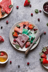 Colourful pancakes on a plate with berries, honey and powdered sugar. Top view