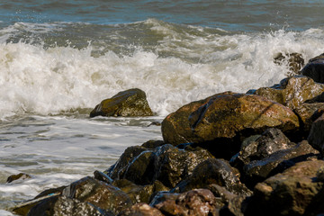Big waves beat against a stone shore on an autumn day. Boulders by the sea against the backdrop of a stormy ocean. Cliffs in the foreground, the water in the background. Concept of windy bad weather
