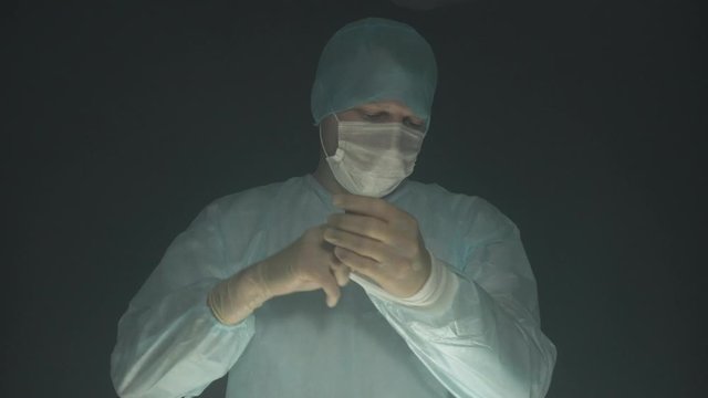 Tired surgeon takes off his gloves, mask and hat after operation or procedure in hospital.