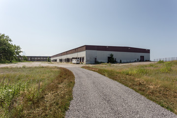 Fototapeta na wymiar Large abandoned warehouse with gravel driveway on nice day