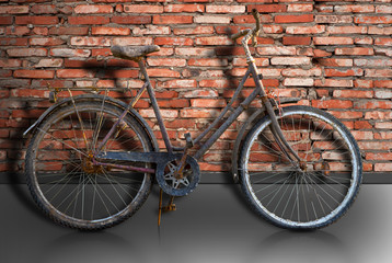 Fototapeta na wymiar Rusty bike parked by brick wall, with reflection in street