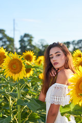 Beautiful young girl enjoying nature on a field of sunflowers. Sunlight plays on the field. Outdoor lifestyle. Summer cozy mood.