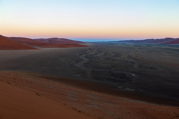Fototapeta na wymiar The rising sun illuminating the mighty dunes of the sossusvlei, as seen from dune 45, in Nambia.