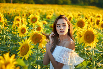 Beautiful young girl enjoying nature on a field of sunflowers. Sunlight plays on the field. Outdoor lifestyle. Summer cozy mood.