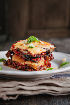 tradicional Parmigiana di melanzane: baked eggplant - italy, sicily cousine.Baked eggplant with cheese, tomatoes and spices on a white plate. A dish of eggplant is on a wooden table