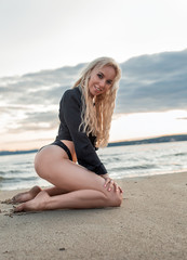 Slim sexy blonde girl kneeling on the beach at sunset