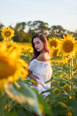 Beautiful young girl enjoying nature on a field of sunflowers. Sunlight plays on the field. Outdoor lifestyle. Summer cozy mood.