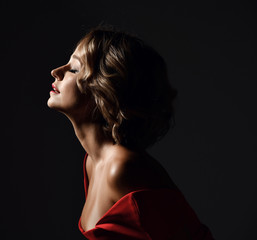 Beautiful trendy woman with curly hair and emotions in red dress posing on dark 