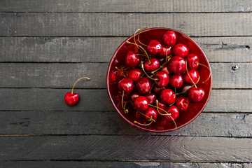 Fresh, ripe cherries in a red glass bowl on black wooden board table background . View from above with copy space