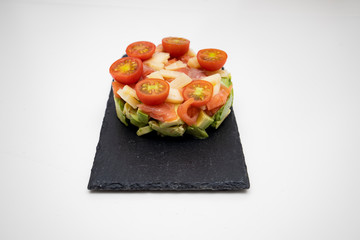 salmon tartar with cheese, avocado and tomatoes on a black plate