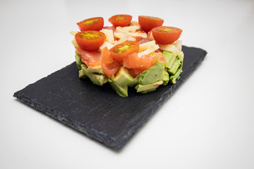 salmon tartar with cheese, avocado and tomatoes on a black plate