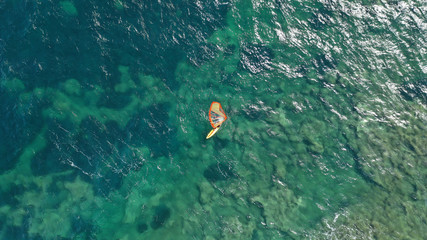 Aerial top view photo of fit man practising wind surfing in Mediterranean bay with crystal clear emerald sea on a windy day