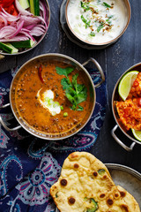 Indian curry meal with black lentils dal, spicy potatoes, rice, naan bread and raita