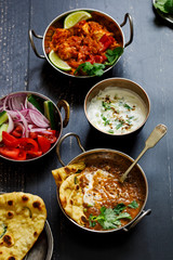 Indian curry meal with black lentils dal, spicy potatoes, rice, naan bread and raita