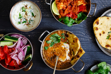 Indian curry meal with black lentils dal, spicy potatoes, rice, naan bread and raita