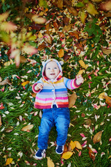 Girl sitting on the grass and playing with colorful autumn leaves