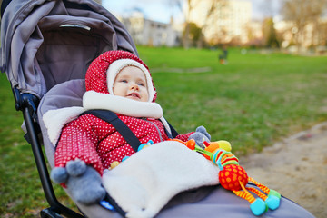 girl in red jacket and white knitted hat and scarf sitting in pushchair