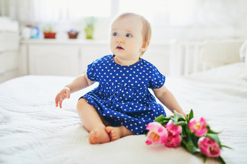 Fototapeta premium Baby girl in blue dress playing with bunch of pink tulips