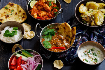 Indian curry meal with black lentils dal, spicy potatoes, rice, naan bread and raita