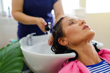 Obraz na płótnie Canvas Hairdresser washing hair of woman female customer with a shower at the saloon applying shampoo on wet hair