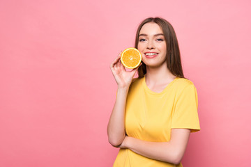 smiling attractive girl holding cut orange and looking at camera on pink
