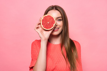 front view of attractive smiling young woman holding cut grapefruit isolated on pink