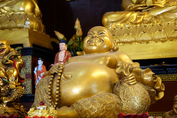Golden sculpture of Laughing Buddha (Budai, Hotei or Pu-Tai) in Taoist temple. God of lucky and happiness. Selective focus.