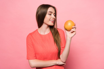 attractive smiling young woman holding grapefruit on pink