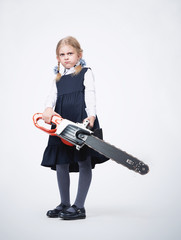 Fototapeta premium Little displeased confident girl in school uniform holds a working electric saw in her hands. Education concept.