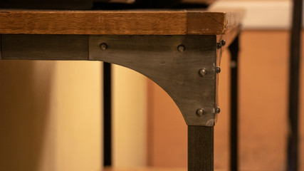 A close up corner of a vintage wooden desk with silver metal brackets holding the legs onto the...