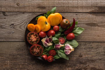 top view of plate with spinach, garlic, chilli pepper and sliced tomatoes on wooden table
