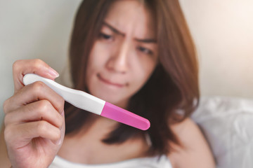 Unhappy young asian woman holding pregnancy test showing a positive result, Wellness and healthy concept, Abortion problem, Selective focus.