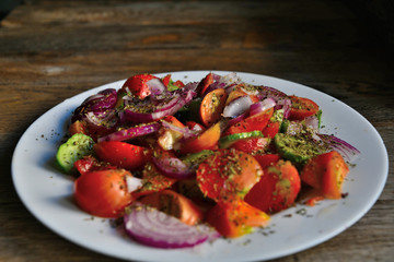 Summer salad of tomatoes, cucumbers, spices and herbs in a white plate on a wooden table.