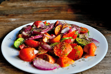 Summer salad of tomatoes, cucumbers, spices and herbs in a white plate on a wooden table.