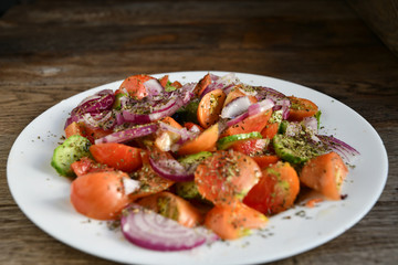 Summer salad of tomatoes, cucumbers, spices and herbs in a white plate on a wooden table.