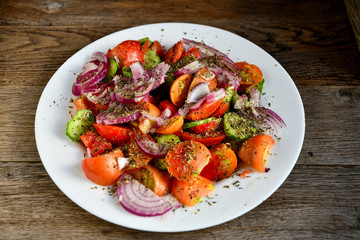 Summer salad of tomatoes, cucumbers, spices and herbs in a white plate on a wooden table.