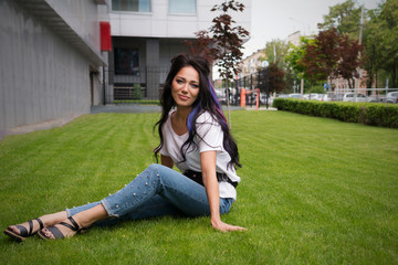 Beautiful young woman sitting on field in green grass. Enjoy nature and fresh air among the city...