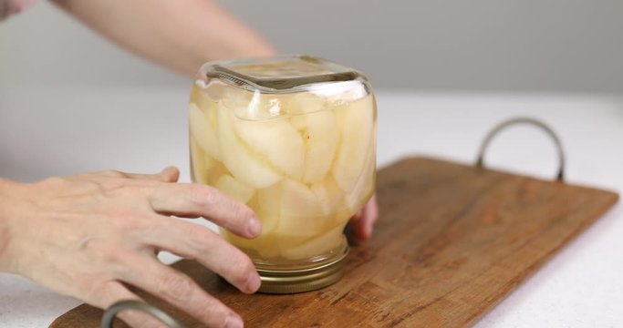 Turning glass jar with boiled sliced peaches upside down to create vacuum