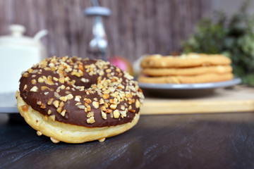 Tasty looking home baked donut with chocolate glazing and nut sprinkles arranged with blurry pastry in background