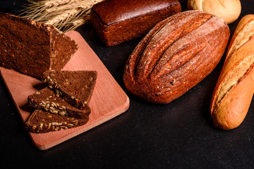 Fresh fragrant bread with grains and cones of wheat against a dark background. Assortment of baked bread on wooden table background. Fresh fragrant bread on the table. Food concept. 
